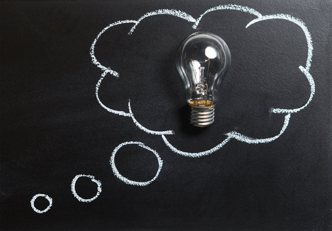 services-04 Light bulb laying on chalkboard with drawn thought bubble, symbolizing creative ideas.