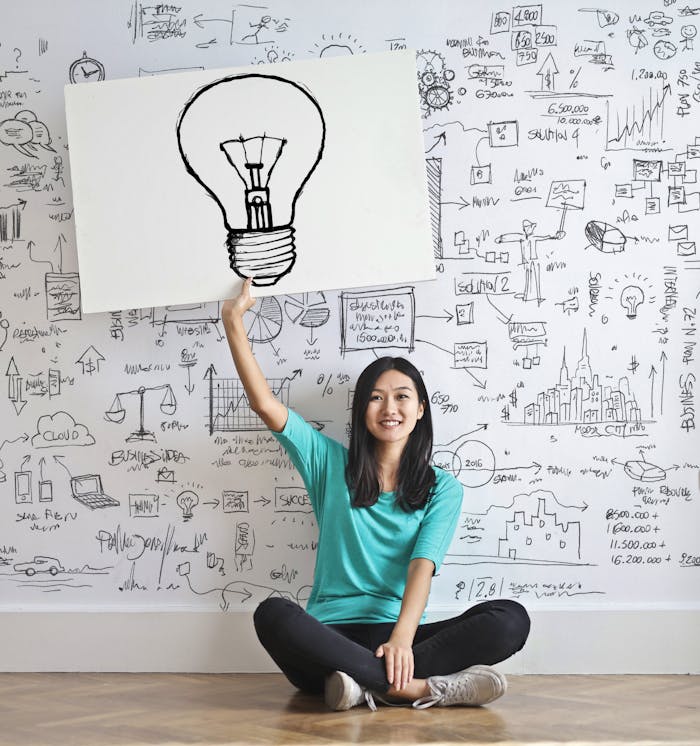 services-03 Young woman holds a light bulb drawing against a creative brainstorming wall.